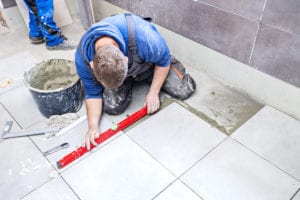 worker laying tile in a bathroom remodel job